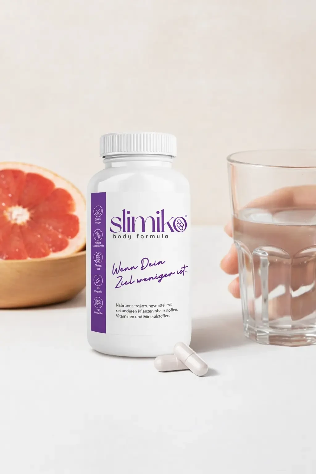 Slimiko Kapseln zur Einnahme mit einem Glas Wasser neben einer aufgeschnittenen Grapefruit